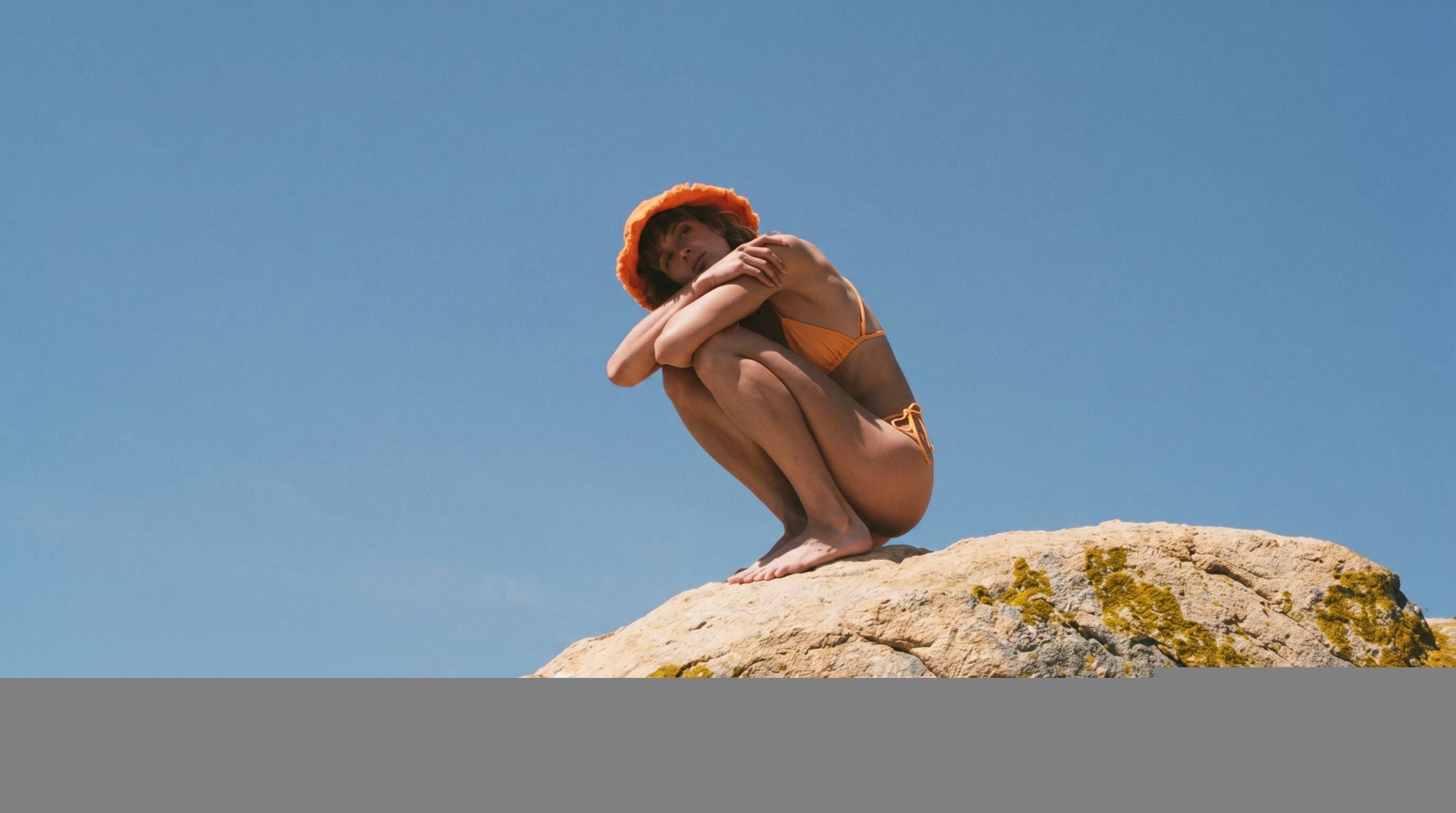 Woman in an orange sun hat on a rock under clear sky